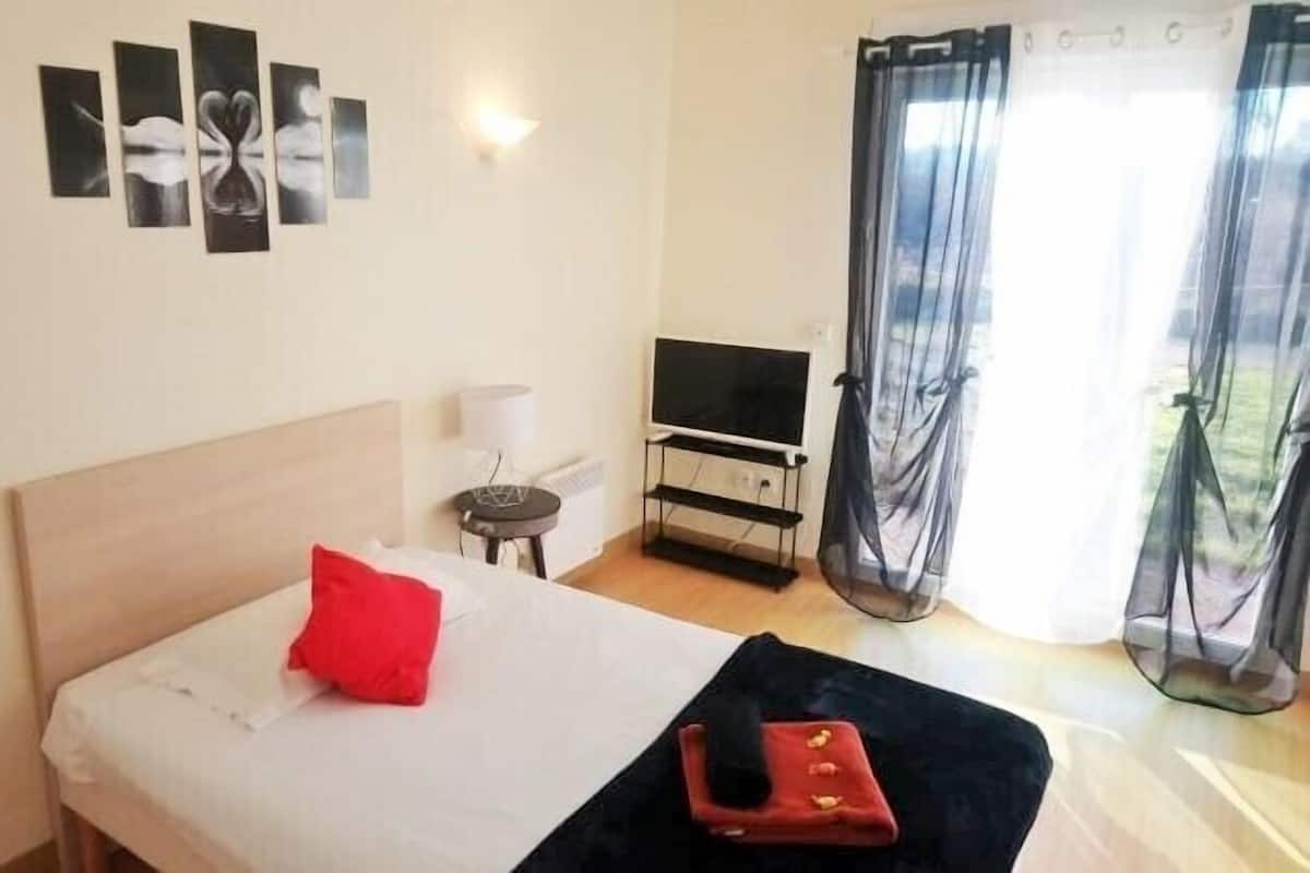 Una habitación de hotel con cama, televisión, una mesita y ventana con cortinas.