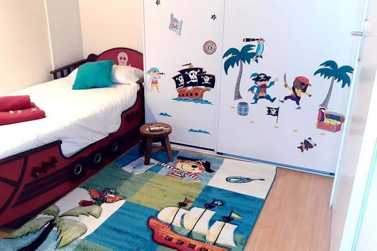 Un dormitorio con una cama, un taburete pequeño y una pared decorada con calcomanías de piratas.