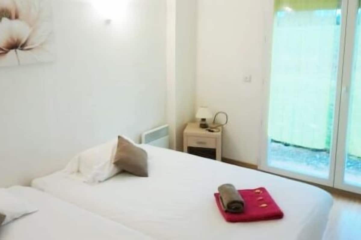 Un dormitorio con cama, almohadas, una mesita de noche, lámpara y ventana con vistas.