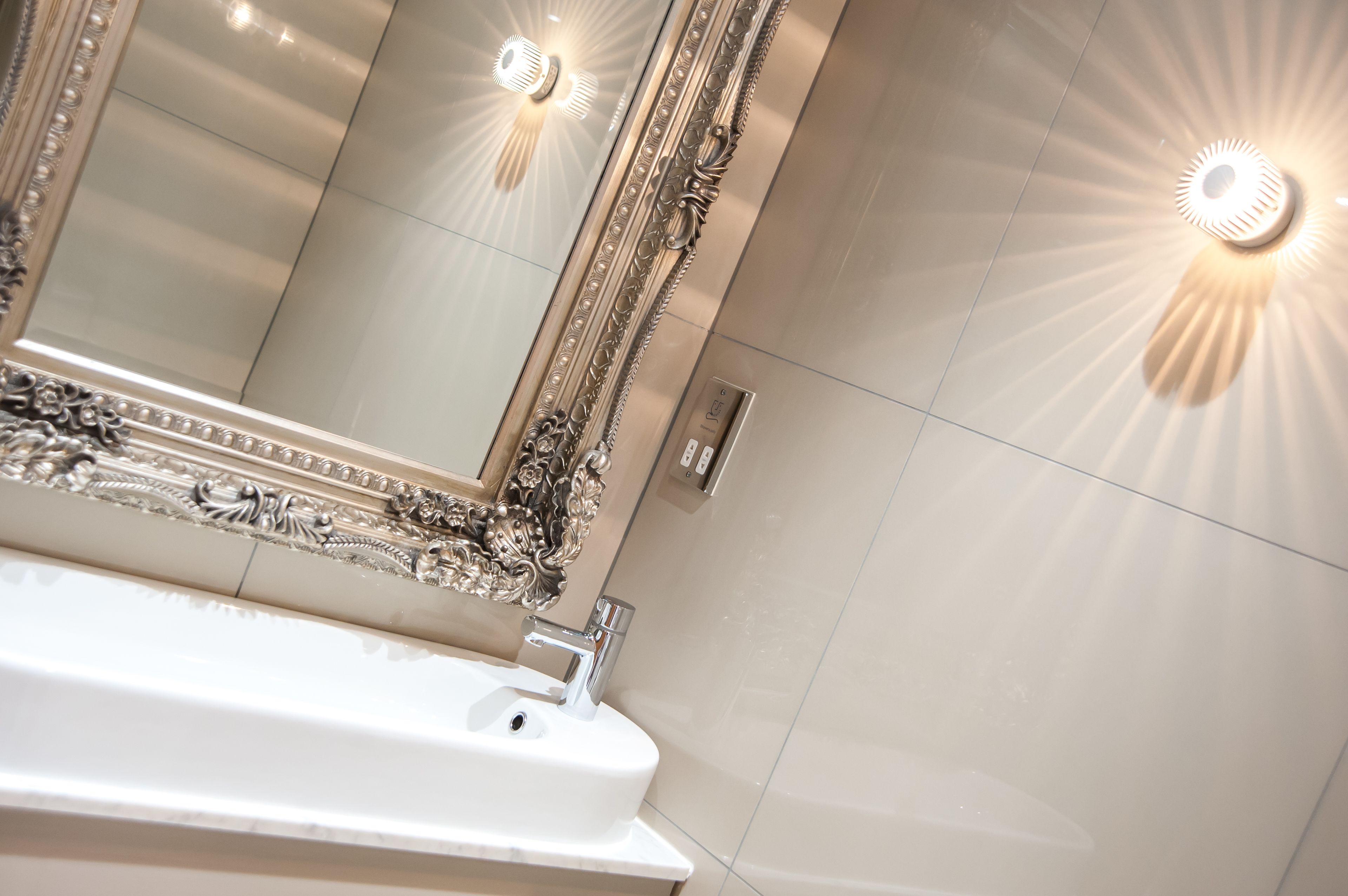 Een badkamer met een grote, sierlijke spiegel, een witte wasbak en wandlampen.