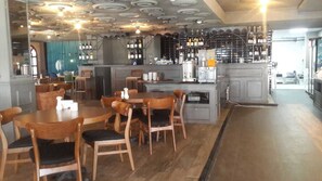 A restaurant with wooden tables and chairs, a bar area with shelves of bottles, and a kitchen in the background. - Borapark Hotel (Aziziye)