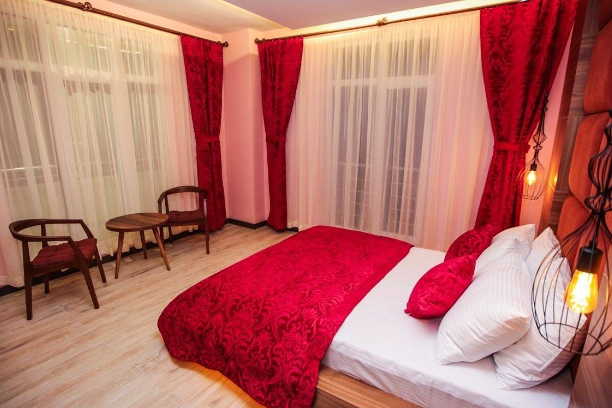 A bedroom with a large bed, red curtains, a wooden chair, and a table.