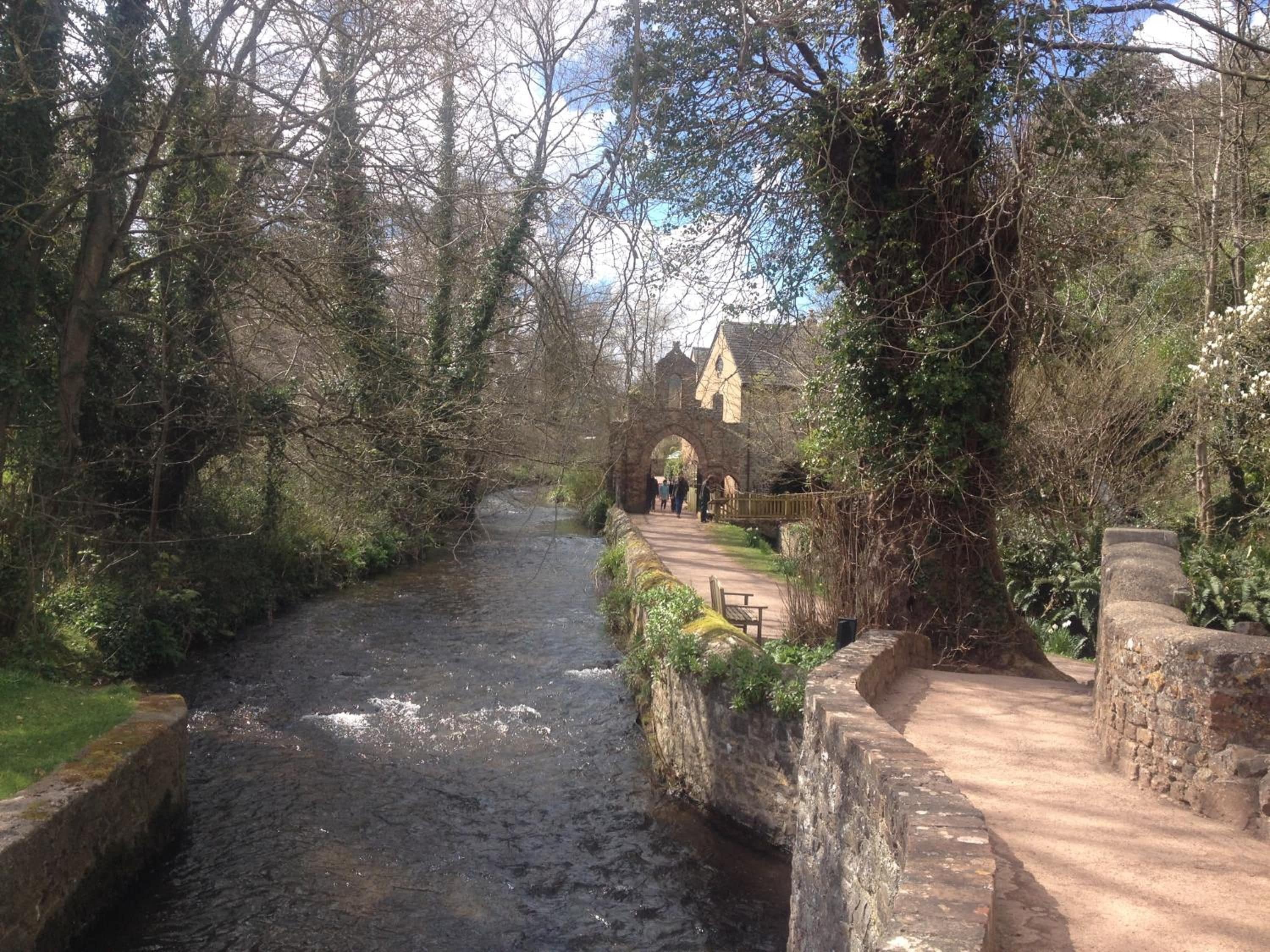 A narrow waterway flanked by stone walls and trees, leading to a historic building with an arched entrance.