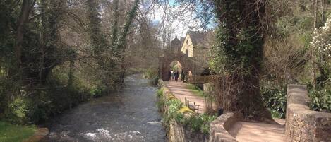 A narrow waterway flanked by stone walls and trees, leading to a historic building with an arched entrance.