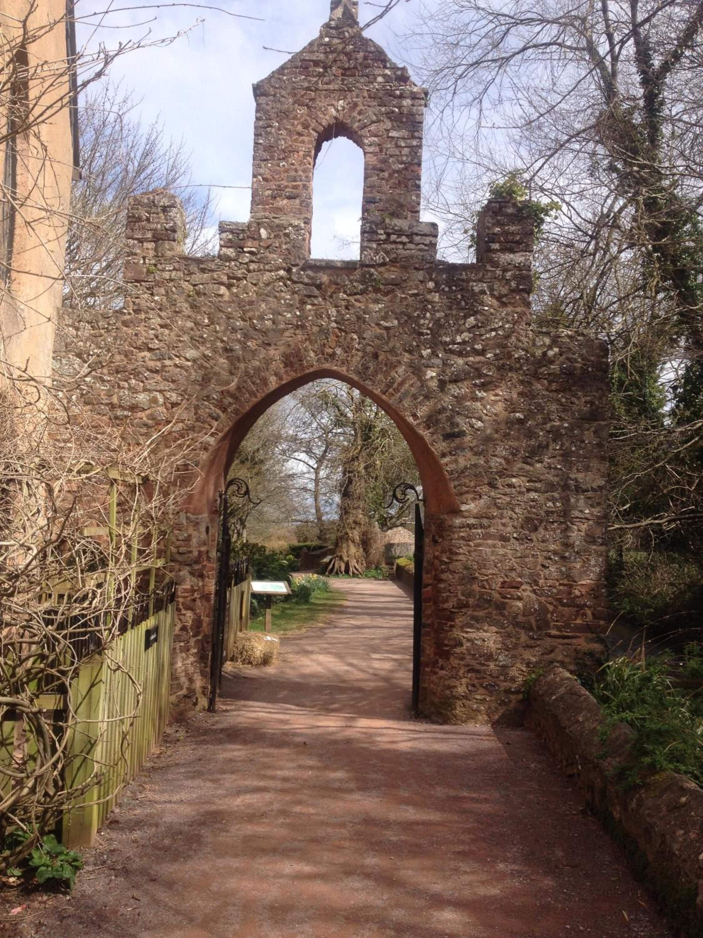 A stone archway leading to a building with a tower.