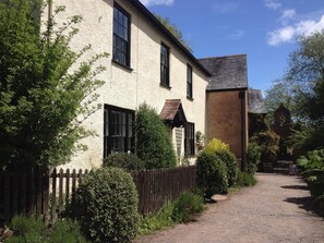 Un bâtiment traditionnel avec une allée de gravier, une clôture en bois et une végétation luxuriante.