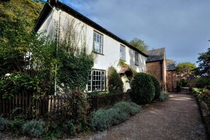 A traditional house with a gravel path leading to the entrance, surrounded by dense greenery and a wooden fence. - Dunster Mill House (Minehead)