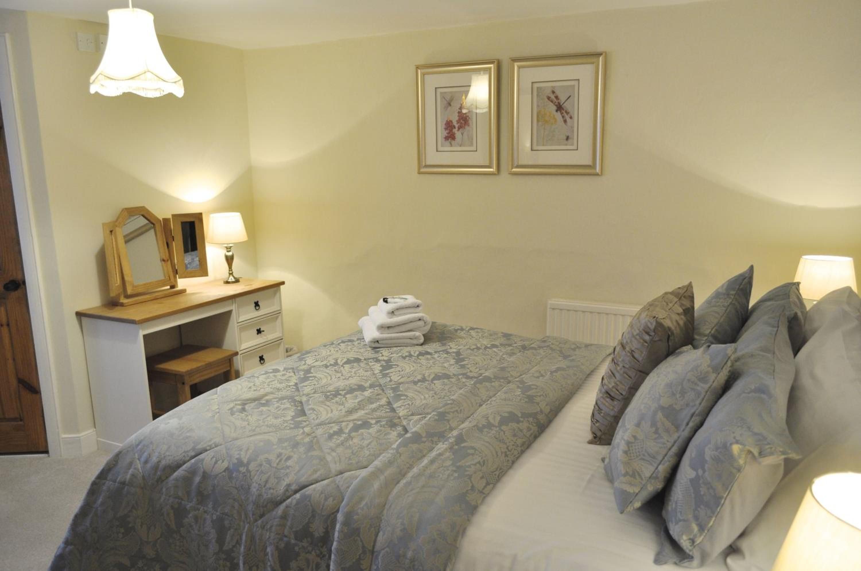 A bedroom with a bed, pillows, a bedside table with a lamp, a dresser, and two framed pictures on the wall.