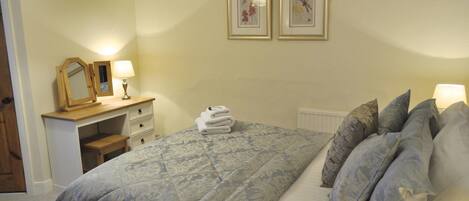 A bedroom with a bed, pillows, a bedside table with a lamp, a dresser, and two framed pictures on the wall.