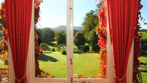 A window with red curtains and a view of a grassy landscape with trees and hills.
