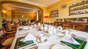 A dining area with a table set for a meal, chairs, a fireplace, and a wall with decorative plates.