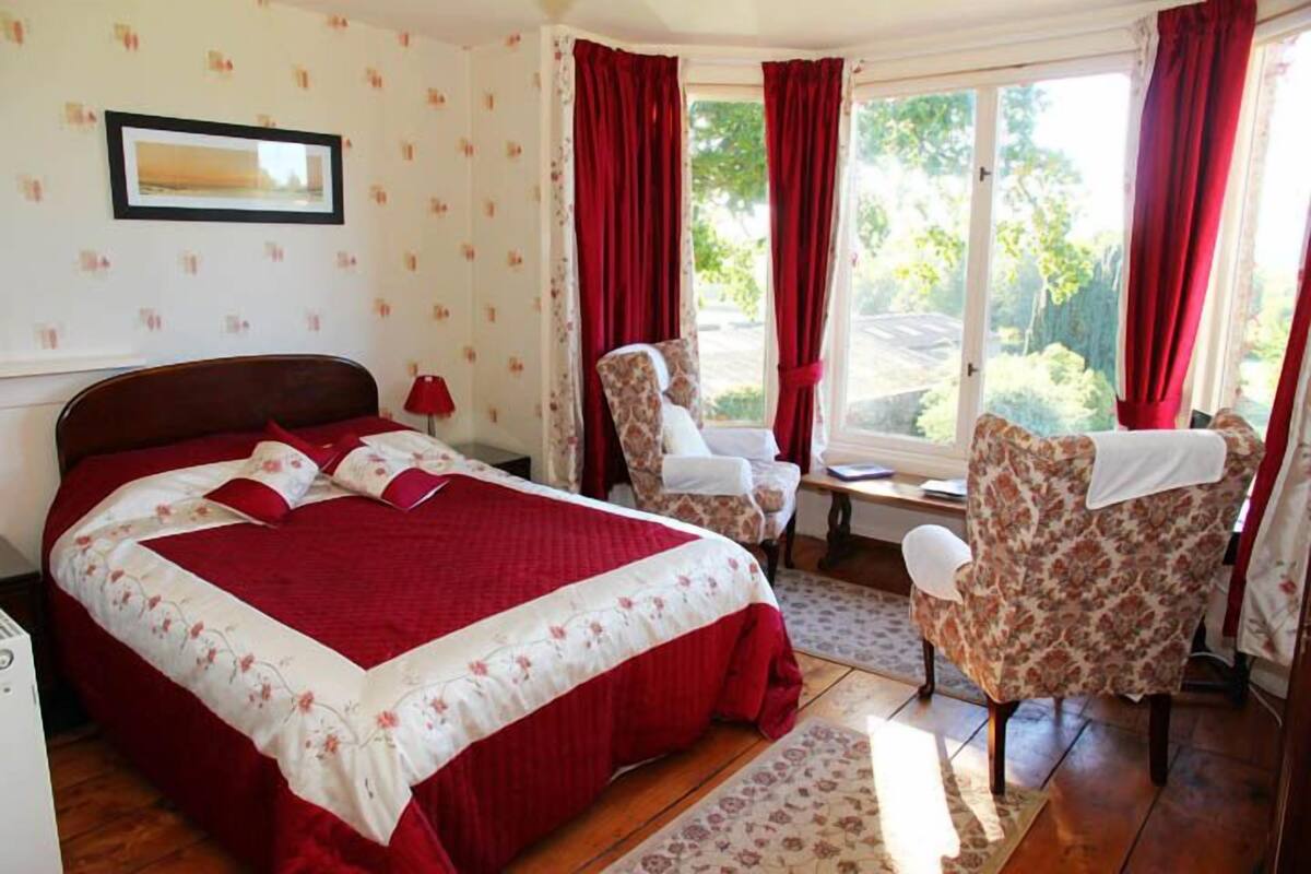 A bedroom with a large bed, a chair, and a window with curtains.