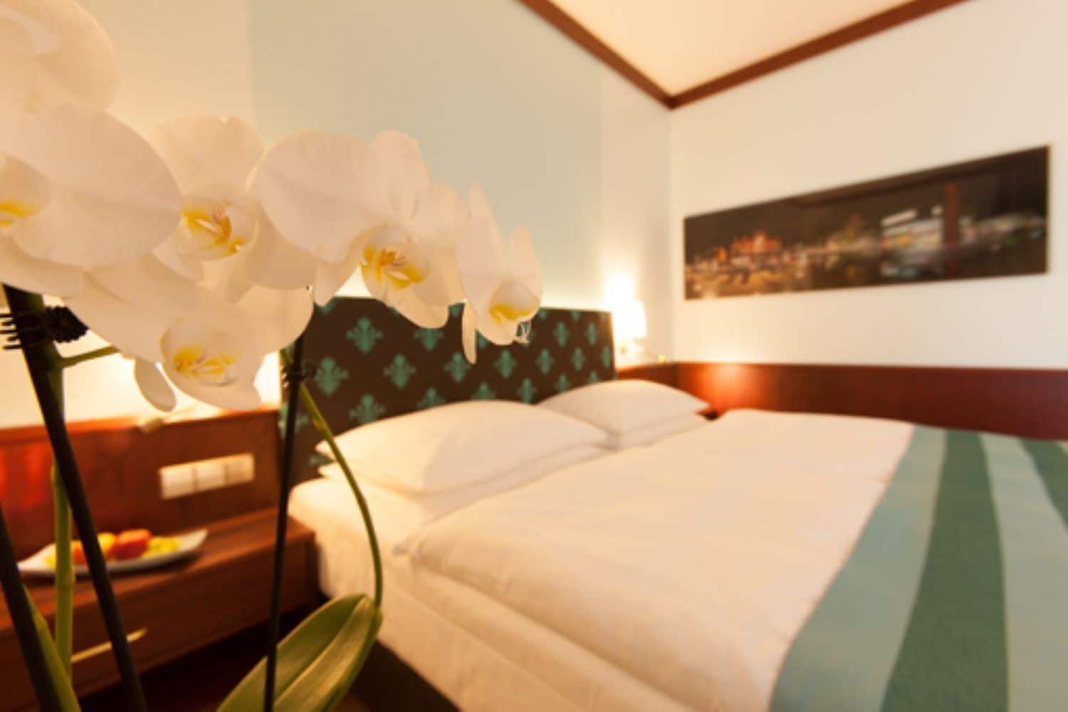A hotel room with a bed, a nightstand with a lamp, and a wall-mounted painting.