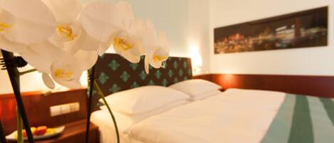 A hotel room with a bed, a nightstand with a lamp, and a wall-mounted painting.