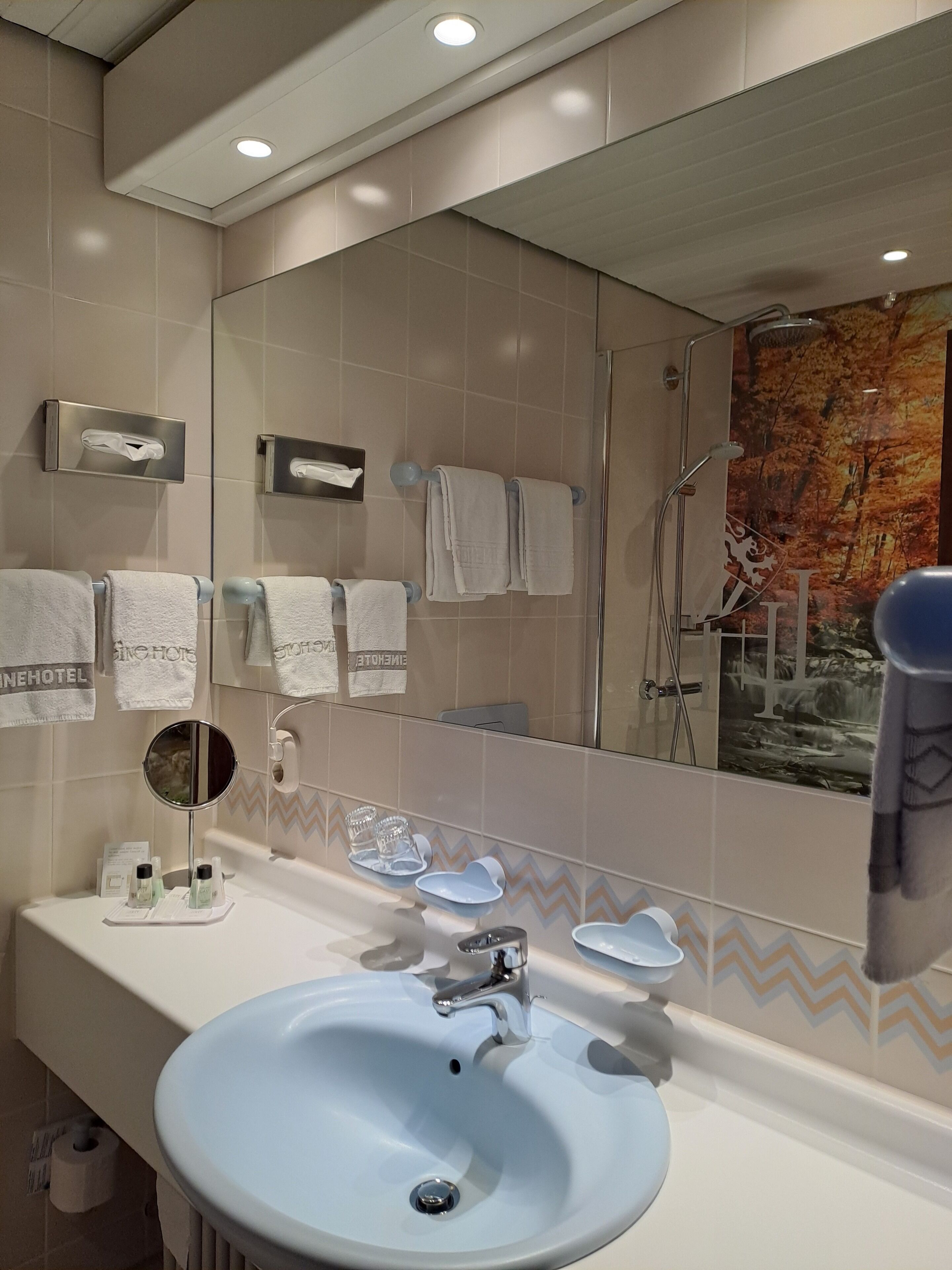 Un baño moderno con un espejo grande, lavamanos blanco y varias toallas.