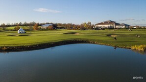 A golf course with a pond, a white building, and a large house in the background. - Leine Hotel (Pattensen)