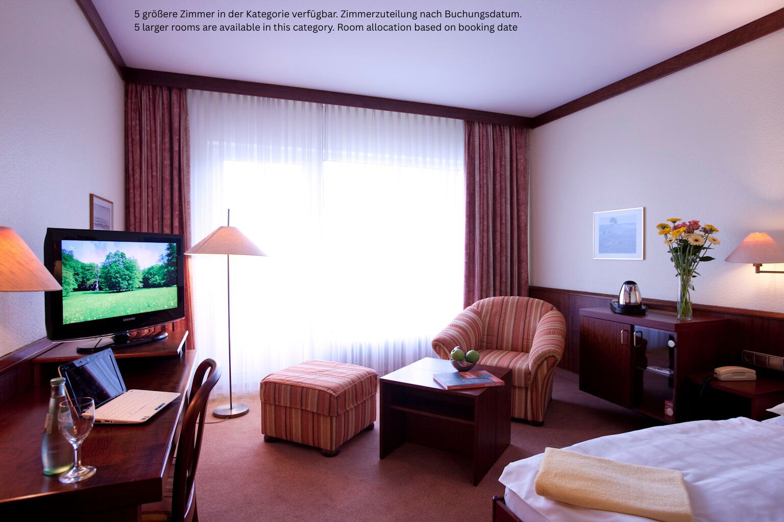 A hotel room with a TV, desk, chair, ottoman, and a bed.