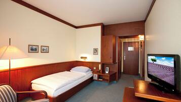 A hotel room with a bed, a desk with a television, a chair, a lamp, and a wardrobe.