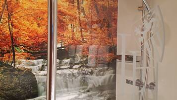Un baño con un mural de cascada, cerramiento de ducha de vidrio y cabezal de ducha cromado.