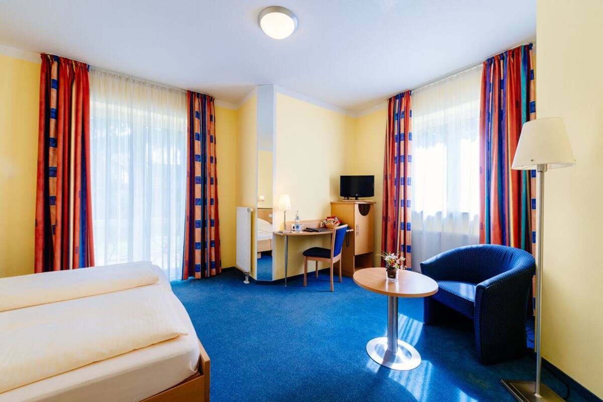 A hotel room with a bed, a desk with a chair, a small table, and a TV.