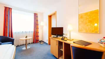 Ein Hotelzimmer mit Bett, Schreibtisch mit Computer, Fernseher, Lampe und einem Fenster mit Vorhängen.