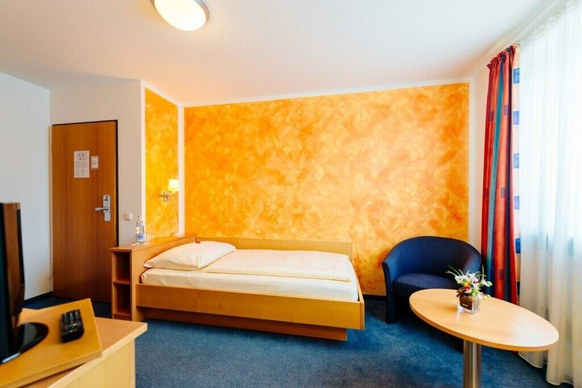 A hotel room with a bed, a chair, a small table, a TV, and a door.