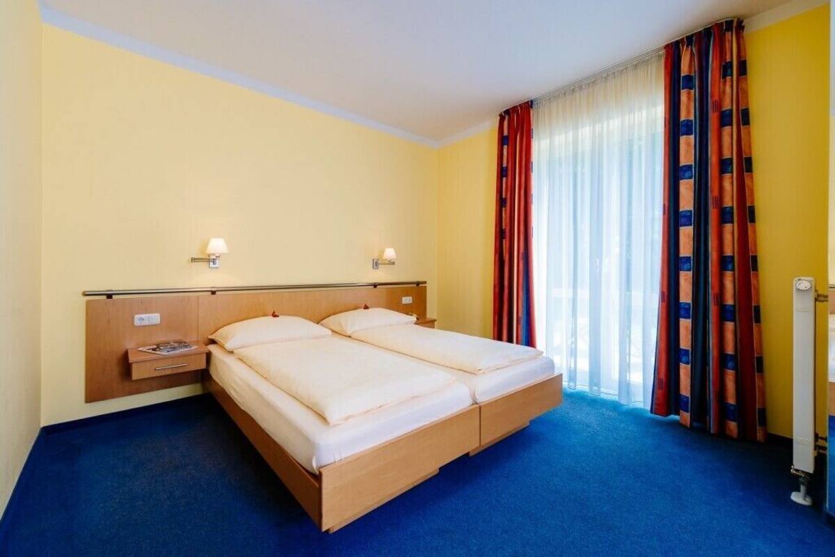 A hotel room with a double bed, two bedside tables, a nightstand, a lamp, and a window with curtains.