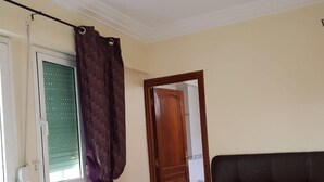 Un dormitorio con cama, ventana con persianas, cortina, puerta y lámpara colgante.