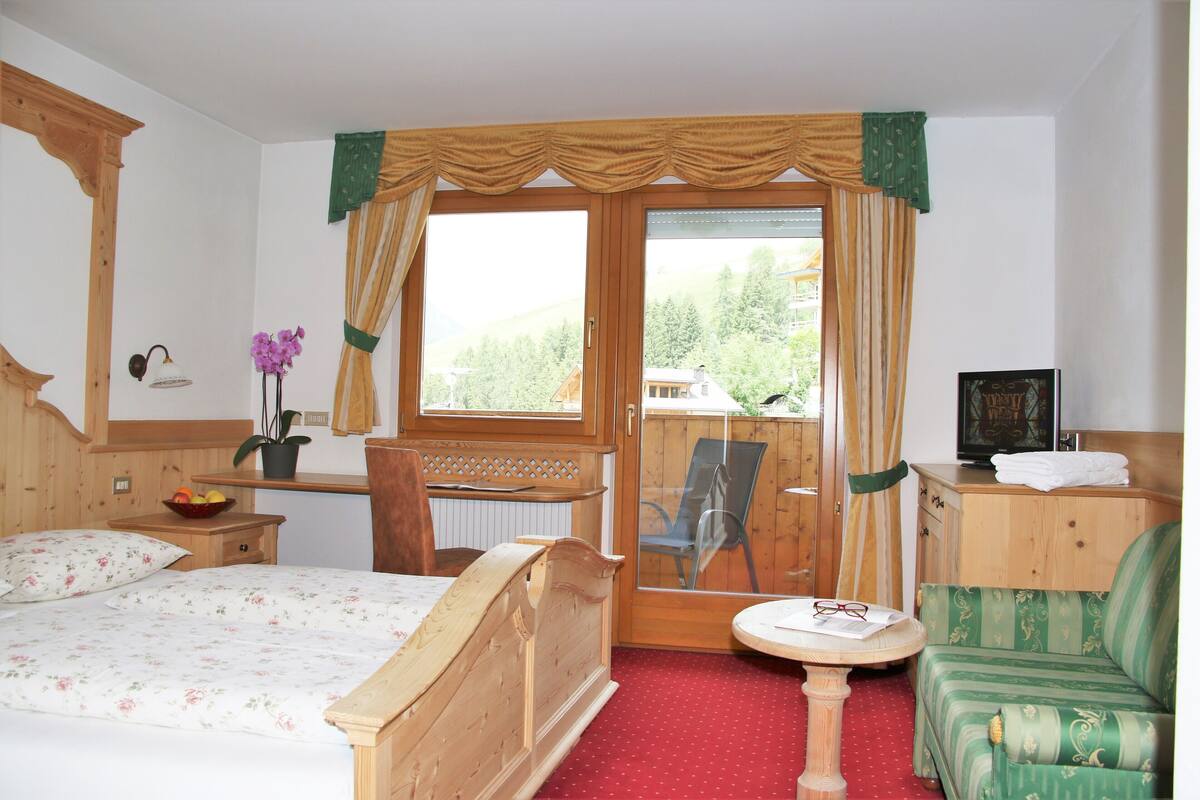 Een slaapkamer met een bed, een bureau, een stoel, een bank en een raam met gordijnen.
