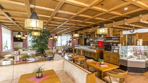 A restaurant interior with wooden beams, hanging pendant lights, and a variety of seating options including booths and tables. - Hotel Alpenrose (La Valle)