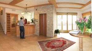 A spacious living area with a wooden staircase, a kitchen counter, and a large window. - Hotel Alpenrose (La Valle)