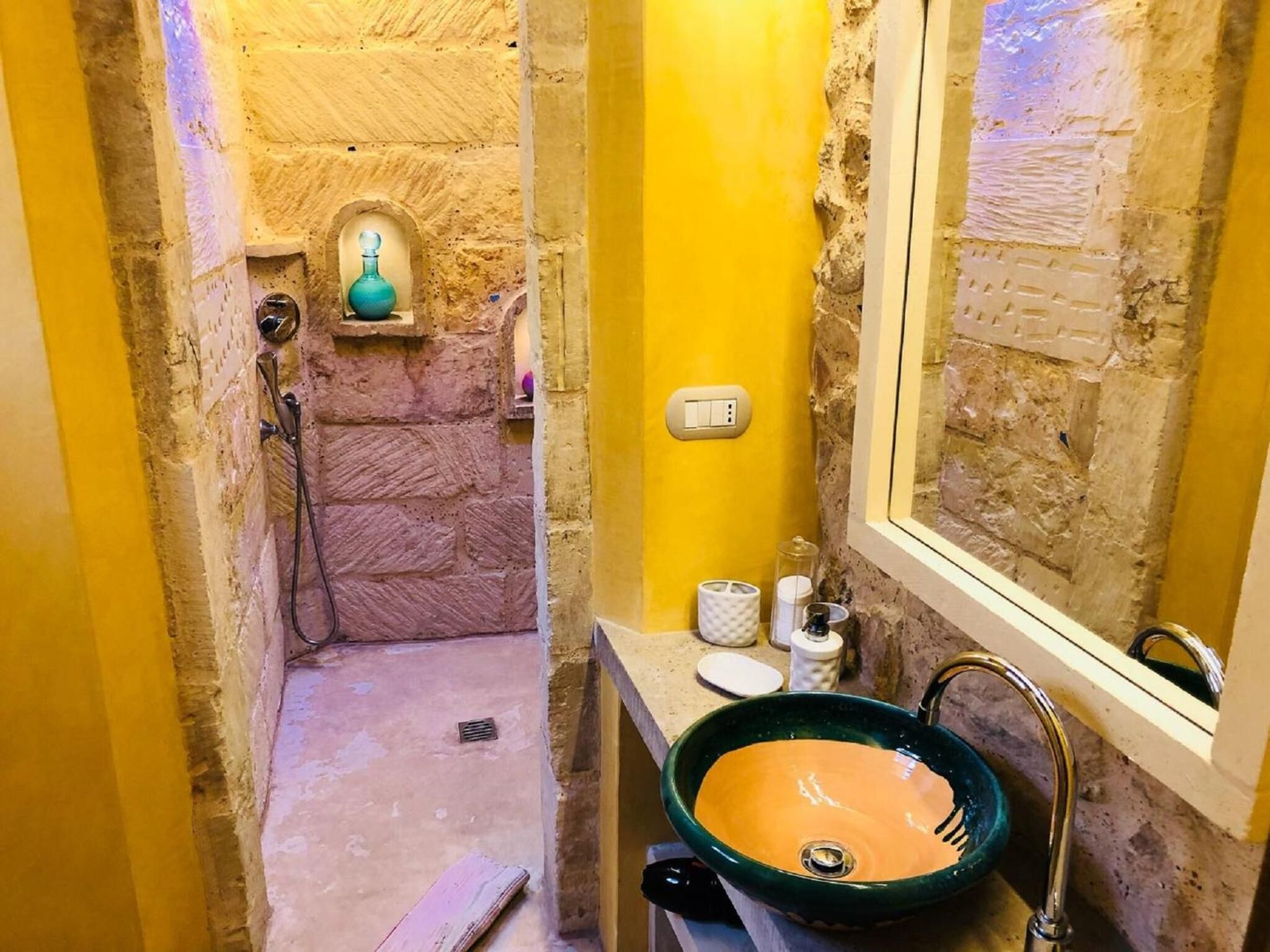 Une salle de bain avec un mur en pierre, un mur jaune, un lavabo vert et un miroir.