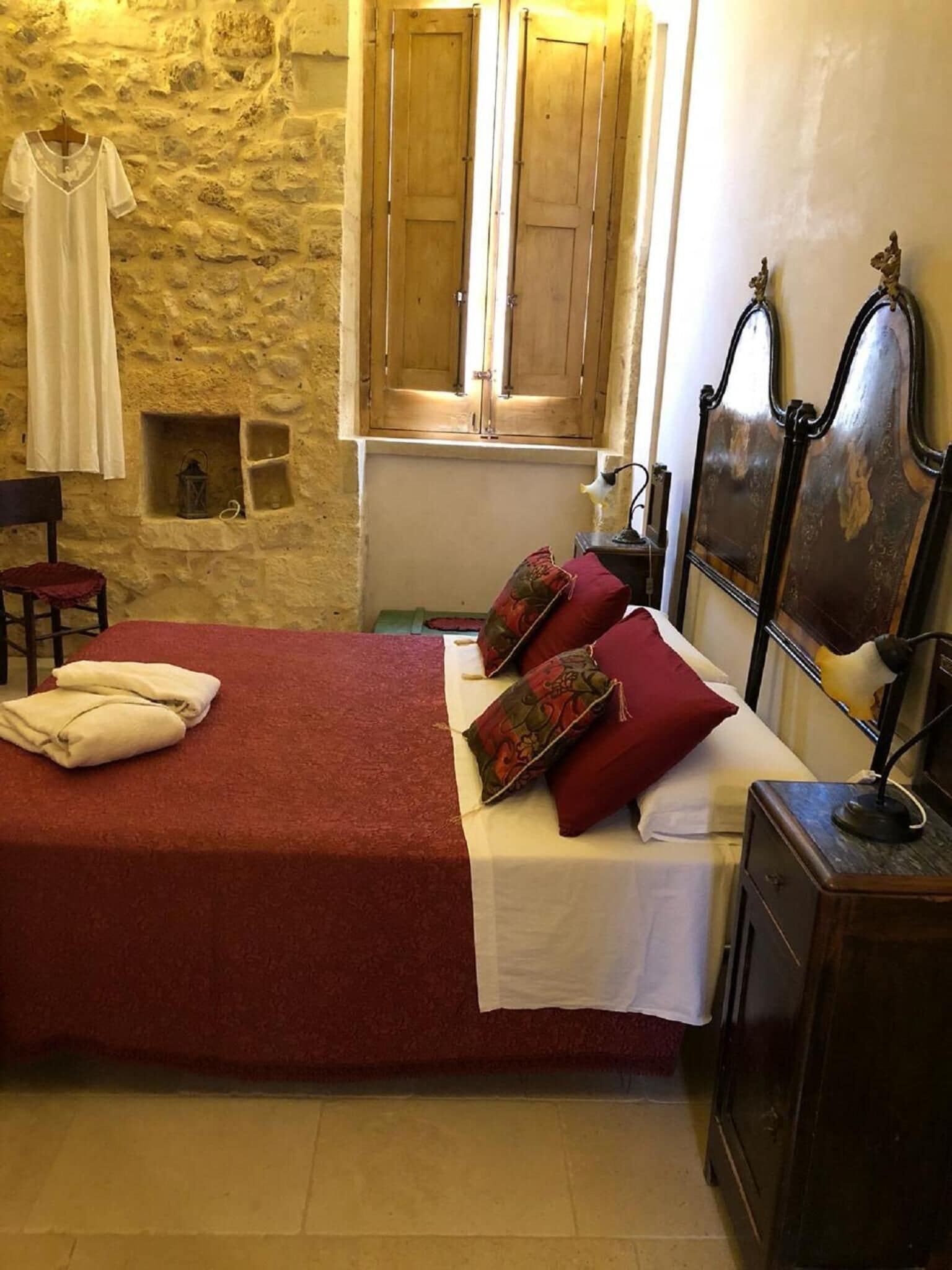 A bedroom with a stone wall, wooden wardrobe, and a bed with red bedding and pillows.