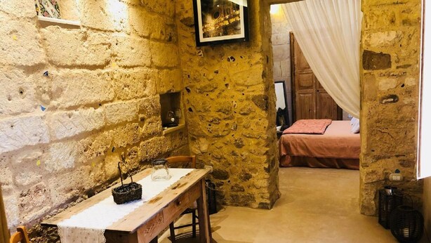 A stone-walled room with a wooden table and bench, a bed with a pink bedspread, and a framed picture on the wall. - Borgoincorte (Martano)