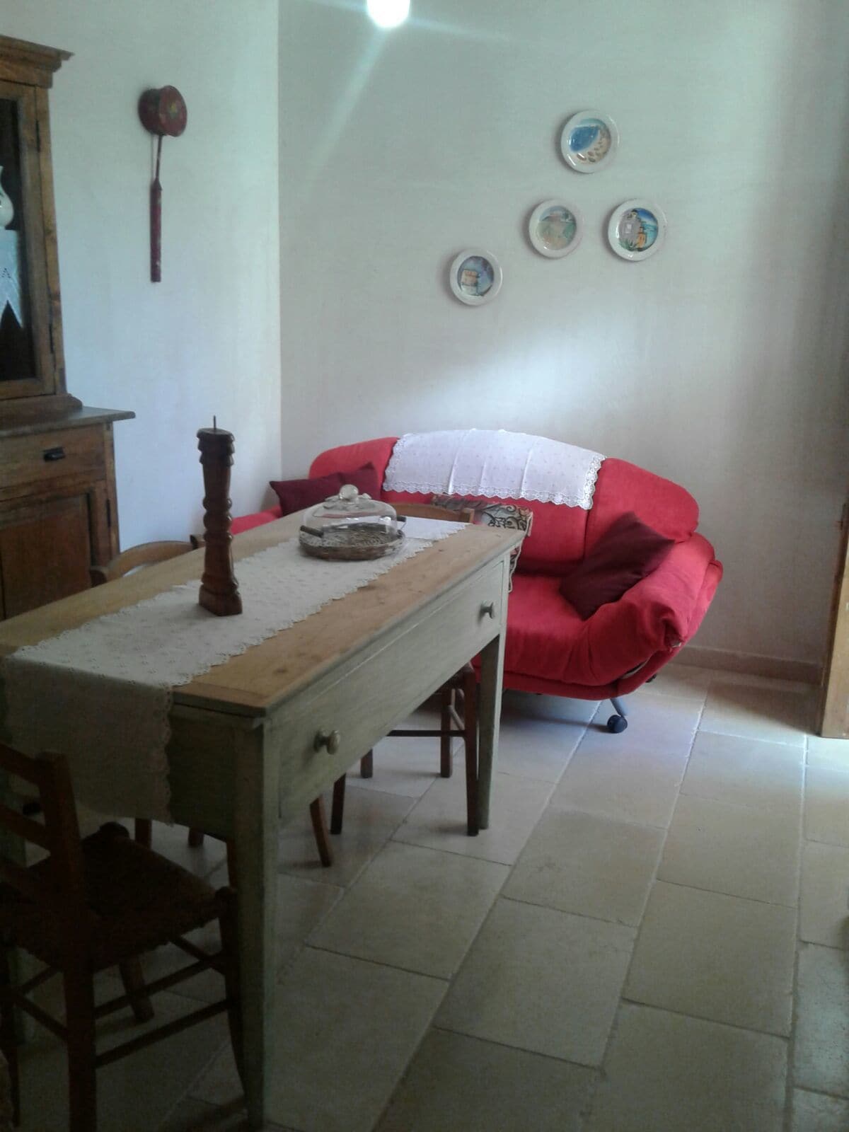 Une pièce avec une table en bois, un canapé rouge et un mur décoré d’assiettes.