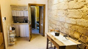 A narrow hallway with a rustic kitchen on one side and a dining area with a table and chairs on the other. - Borgoincorte (Martano)