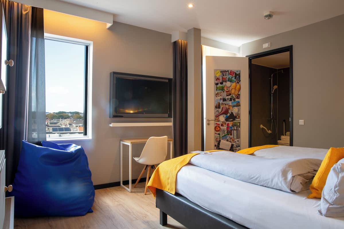 A modern hotel room with a bed, a television, a desk, and a bean bag chair.