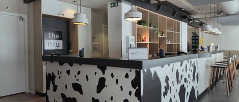 Ein moderner Empfangstresen mit Kuhmuster-Design, einem Schild mit der Aufschrift 'IHG ONE REWARDS' und einer Bar mit Hockstühlen.