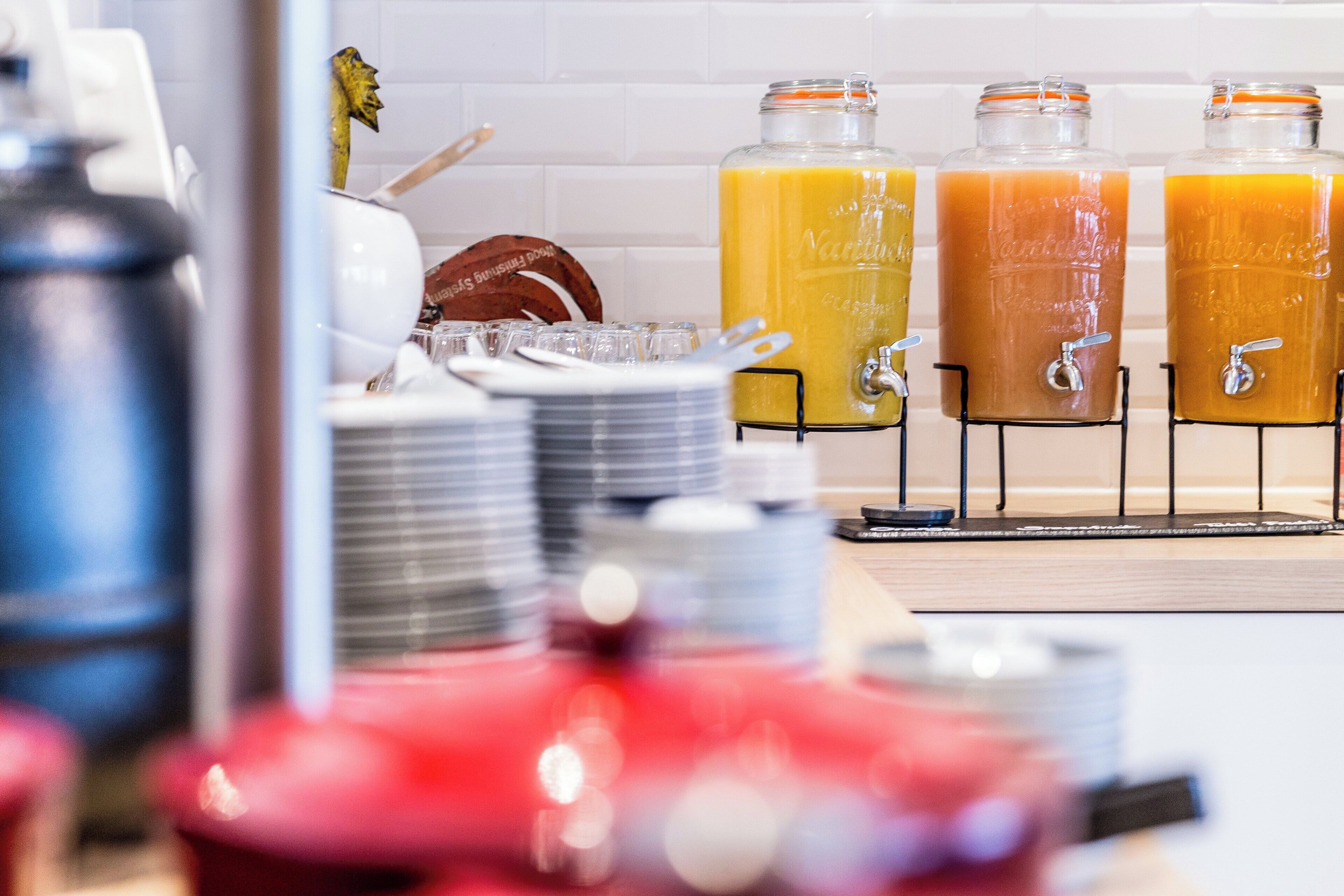 A beverage station with three dispensers, each containing a different colored drink, and a stack of plates in the foreground.