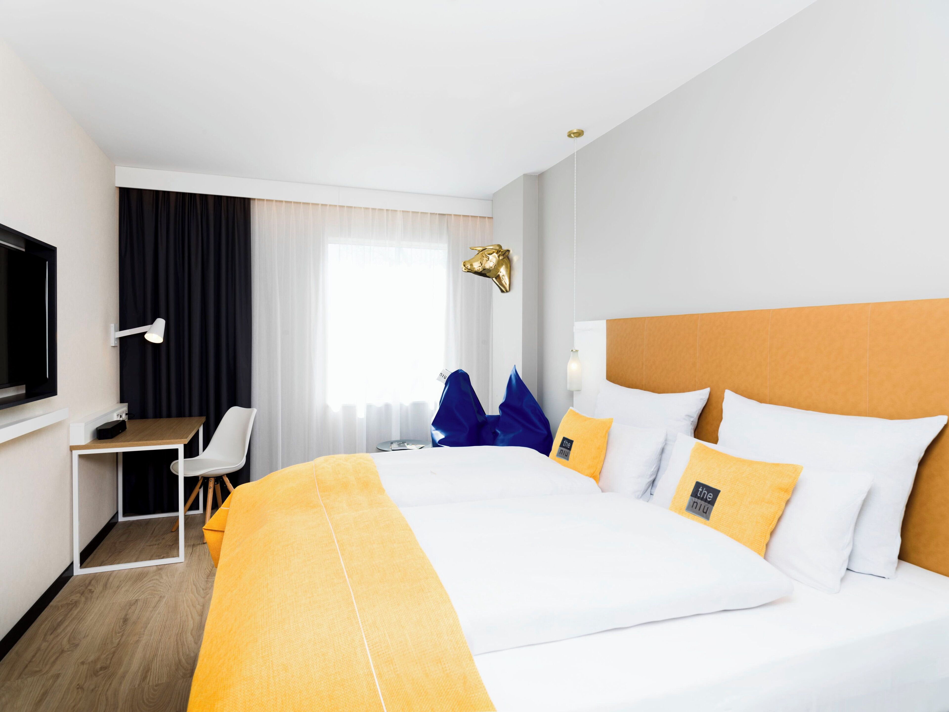 A hotel room with a large bed, a desk, a chair, a television, and a window with curtains.