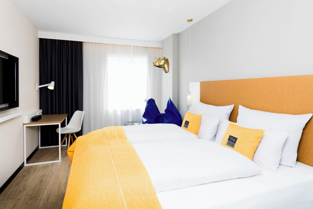 A hotel room with a large bed, a desk, a chair, a television, and a window with curtains.