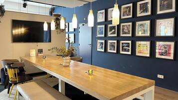 A modern office space with a long wooden table, multiple chairs, and a large flat-screen TV mounted on the wall.