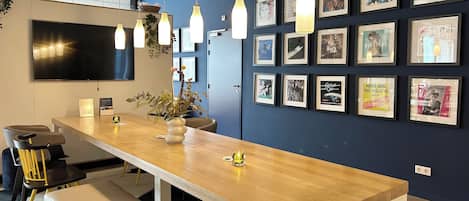 A modern office space with a long wooden table, multiple chairs, and a large flat-screen TV mounted on the wall.