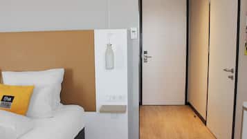 A hotel room with a bed, a bedside table, a wall-mounted light, and a door.