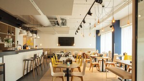 A modern restaurant with a bar area, round tables, and yellow chairs. - Holiday Inn - the niu, Dairy Haarlem by IHG (Haarlem)