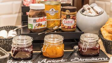 Variedad de frascos y recipientes con mermeladas y conservas, incluyendo marcas como Nutella y Calvé, sobre una bandeja etiquetada con nombres de frutas.