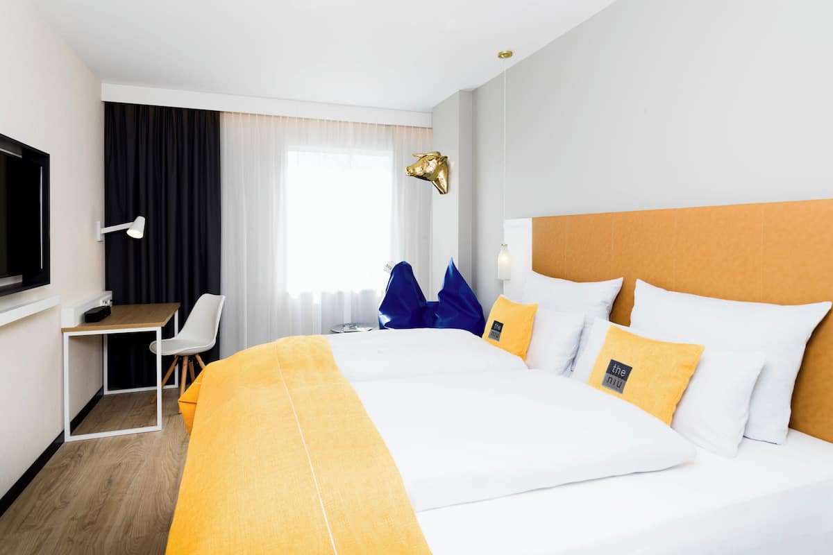 A hotel room with a large bed, a desk, a chair, a television, and a window with curtains.