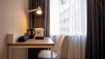 A modern hotel room with a wooden desk, a white chair, a coffee machine, and a lamp.