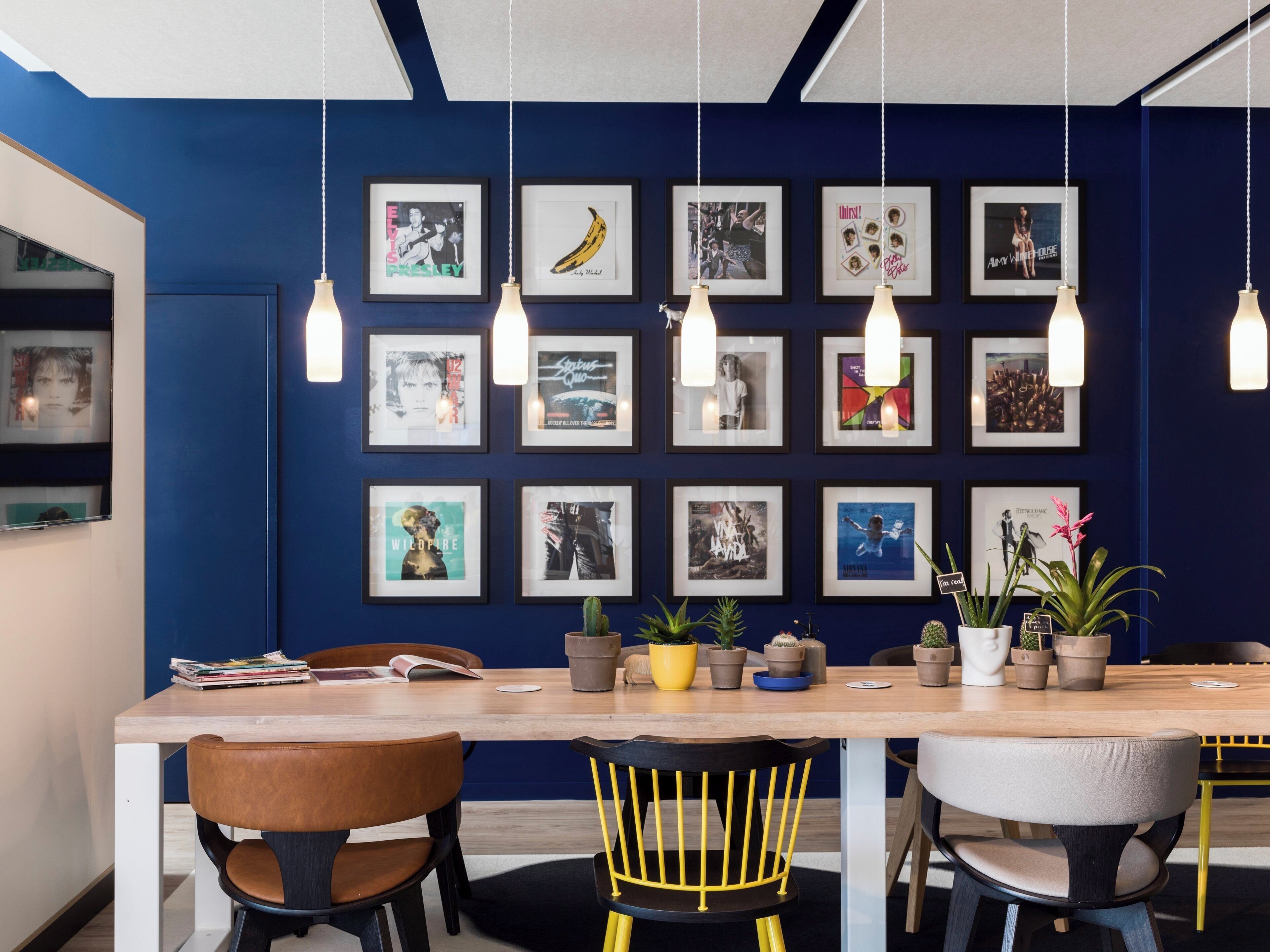 A modern meeting room with a wooden table, multiple chairs, and framed pictures on the wall.