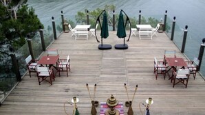 Une terrasse en bois avec des tables et des chaises, un tapis décoratif et une vue sur l’eau.